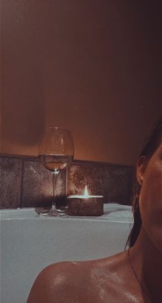 a woman sitting in a bathtub next to a glass of wine and a candle