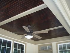 a ceiling fan mounted to the side of a wooden ceiling in a room with windows