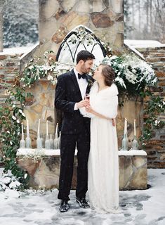 a bride and groom standing in front of a stone fireplace surrounded by greenery with candles