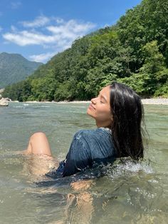 a woman laying on her back in the water with mountains in the background and blue sky