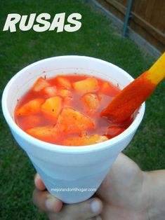 a hand holding a cup filled with soup and an orange carrot sticking out of it