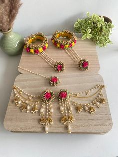 three pieces of jewelry sitting on top of a wooden board next to a potted plant