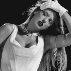 a black and white photo of a woman with her hands on her head while wearing pearls