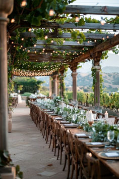 an outdoor dining area with tables and chairs covered in greenery, surrounded by string lights