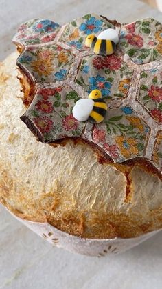 two bees are sitting on top of a loaf of bread that is decorated with flowers and leaves