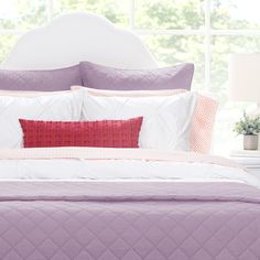 a bed with purple and white comforters in front of a window