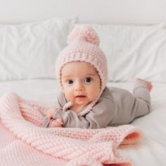 a baby laying on top of a bed wearing a pink knitted hat and blanket