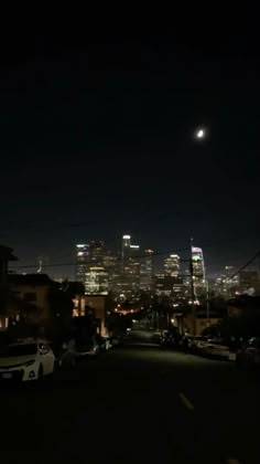 the city skyline is lit up at night, with cars parked on the street below