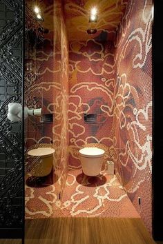 a bathroom with a toilet, sink and mirror in it's stall area that has an intricate design on the wall