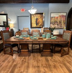 a dining room table and chairs with blue dishes on them in front of a painting