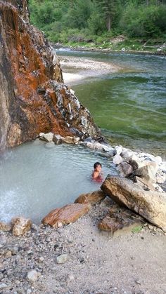 a man swimming in a river next to a rocky cliff