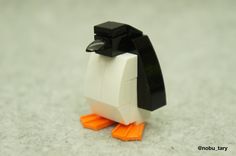 a lego penguin with an orange beak and black head is standing on the floor in front of white carpet