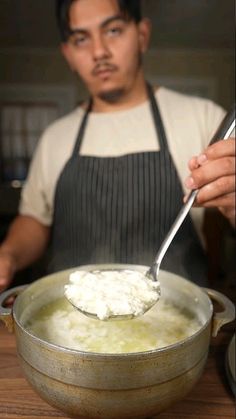 a man in an apron is spooning cottage cheese into a pot