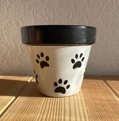 a white and black cup with paw prints on the side sitting on a wooden table