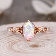 a white opal ring sitting on top of a piece of wood with an intricate design