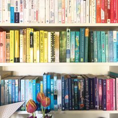 there are many books on the shelves with flowers in vases next to each other