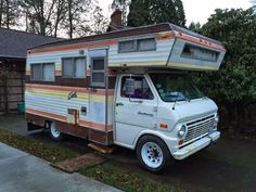 an old camper is parked in front of a house with a roof over it