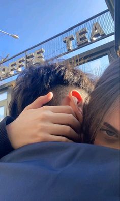 a man with his head on the back of another mans shoulder in front of a sign