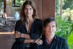 two people standing next to each other in front of a wooden porch with plants and trees