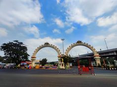 two archways in the middle of an empty parking lot under a cloudy blue sky