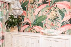 a room with pink and green wallpaper, white cabinets and a basket on top of the cabinet