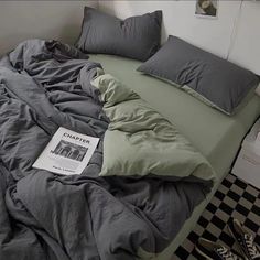 an unmade bed with grey sheets and pillows on top of it, next to a black and white checkered floor