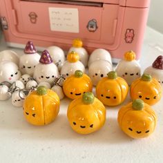 many small pumpkins with faces on them sitting next to a pink box filled with smaller white pumpkins