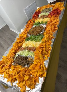 a long table filled with lots of different types of food on tin foil covered in chips