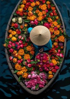 a person in a boat with flowers floating on the water and wearing a straw hat