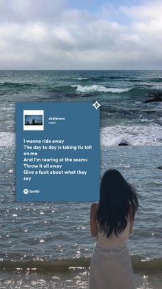 a woman standing on top of a beach next to the ocean holding up a sign