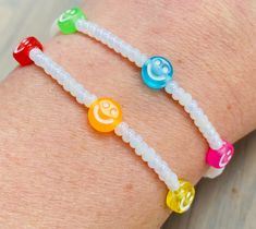 two bracelets with different colored beads and smiley face charms on the wrist are shown