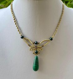 a necklace on a mannequin with a green bead and gold tone pendant