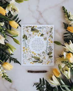 a card surrounded by flowers and greenery on a marble surface with an inscription in the middle