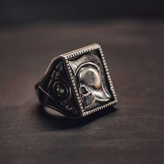 a silver ring with a skull in the center on a black surface, close up