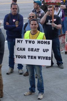 a man holding a sign that says, my two moms can beat up your ten wives