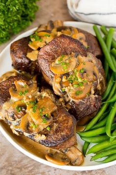 some green beans and mushrooms on a white plate with gravy over the top