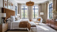 a bedroom with a large bed and two chairs in front of the window, along with a chandelier hanging from the ceiling