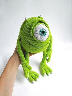 a hand holding up a green knitted frog hat with eyes on it's head