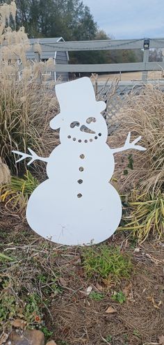 a snowman made out of plywood sitting in the middle of some grass and bushes