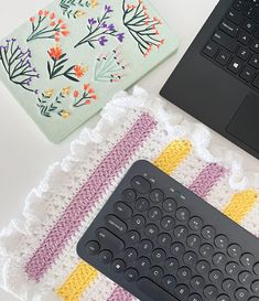 a keyboard, mouse pad and laptop on a white table with colorful crocheted placemats