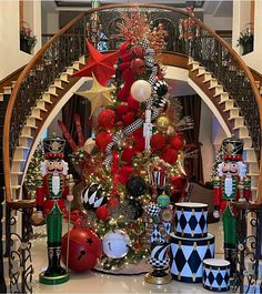 a christmas tree decorated with red, white and black ornaments in front of a staircase