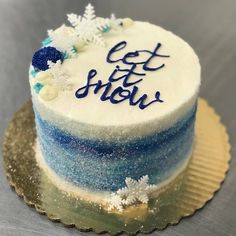 a blue and white cake with let it snow written on the frosting, sitting on a gold plate