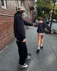 a man and woman are holding hands while standing on a skateboard in front of a brick building