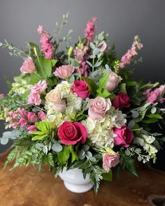 a white vase filled with lots of pink and white flowers on top of a wooden table