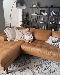 a baby sitting on top of a brown leather couch in front of a book shelf