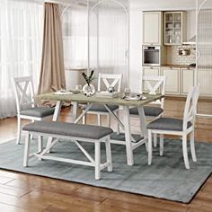 a dining room table with chairs and a bench in front of the window on a rug