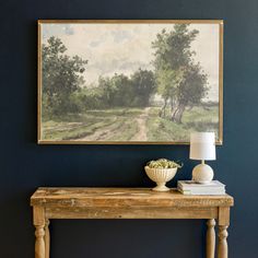 a painting hangs on the wall above a table with a vase and lamp next to it