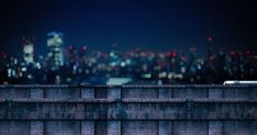 a city skyline is seen in the distance from a brick wall with a bench on it