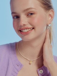 a woman wearing a purple shirt and silver necklace smiling at the camera with her hand on her neck