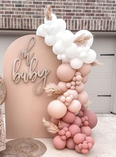 a baby shower sign with balloons and feathers on the top, in front of a brick building